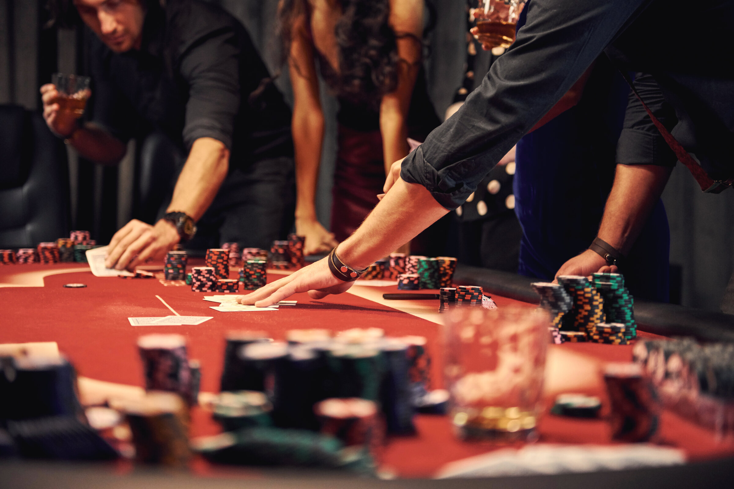Guests in evening wear around a red-felt poker table, chips stacked, warm low light